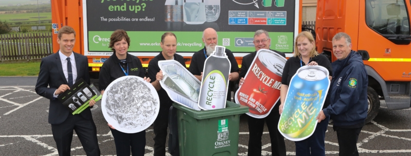A group of representatives from MetalMatters and Orkney Council holding cardboard cut-outs of metal packaging items in front of one of their recycling vehicles which bears the MetalMatters signage artwork.